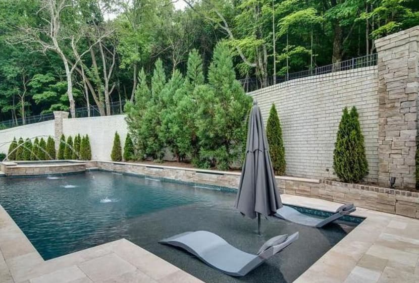 Pool with fountain and lounge chairs by a stone wall
